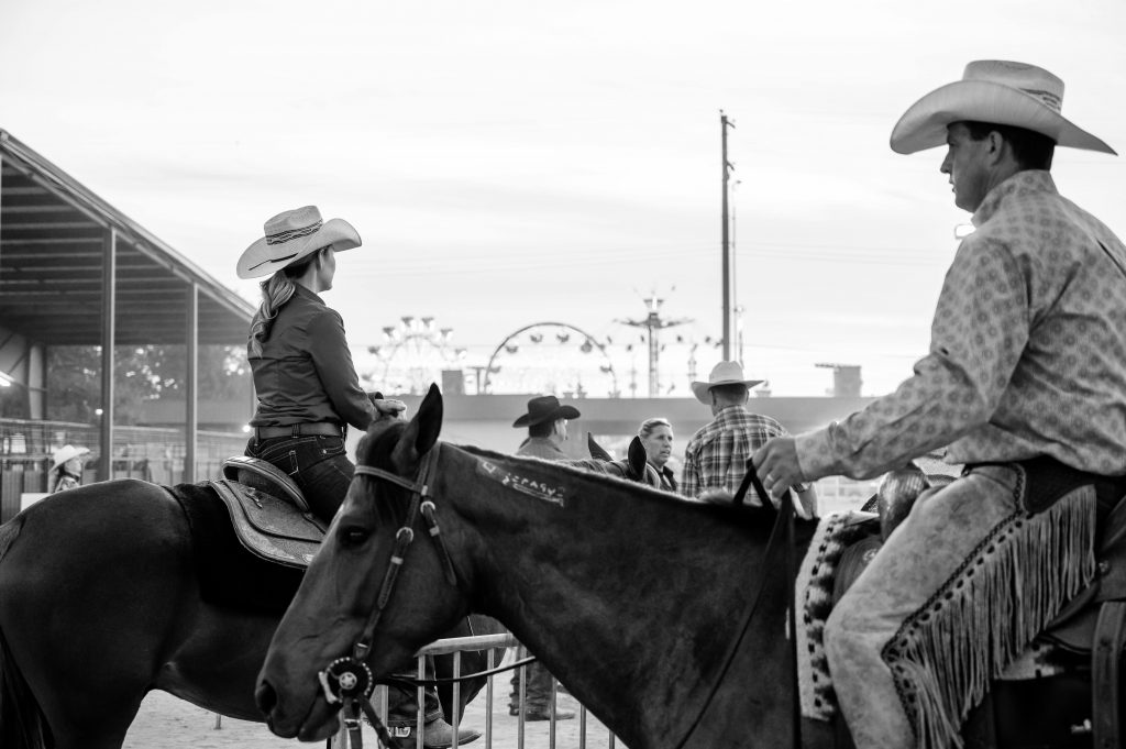 Monochrome image capturing cowboys and horses at a rodeo arena setting.