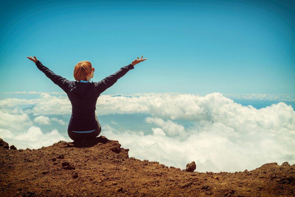 Best Travel Deals on Trip.com: Your Ultimate Guide to Affordable Adventures A woman enjoys a scenic view atop a cliff in Kula, Hawaii, surrounded by clouds and blue sky.