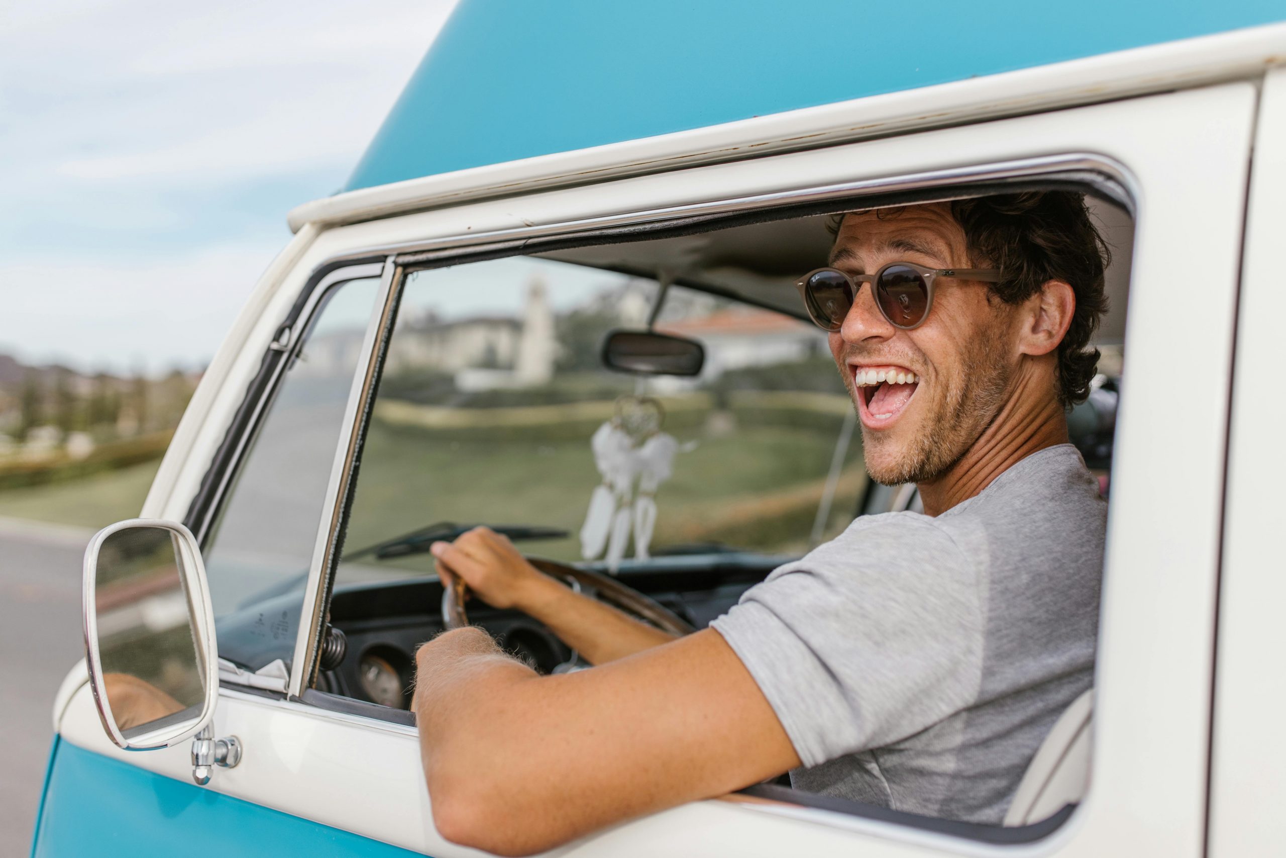 A joyful man in sunglasses drives a vintage campervan on a sunny day.